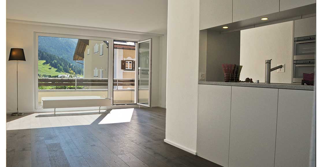 Foto: offene Küche grau mit Einblick ins Wohnzimmer und Aussicht auf Chalett und den Wald